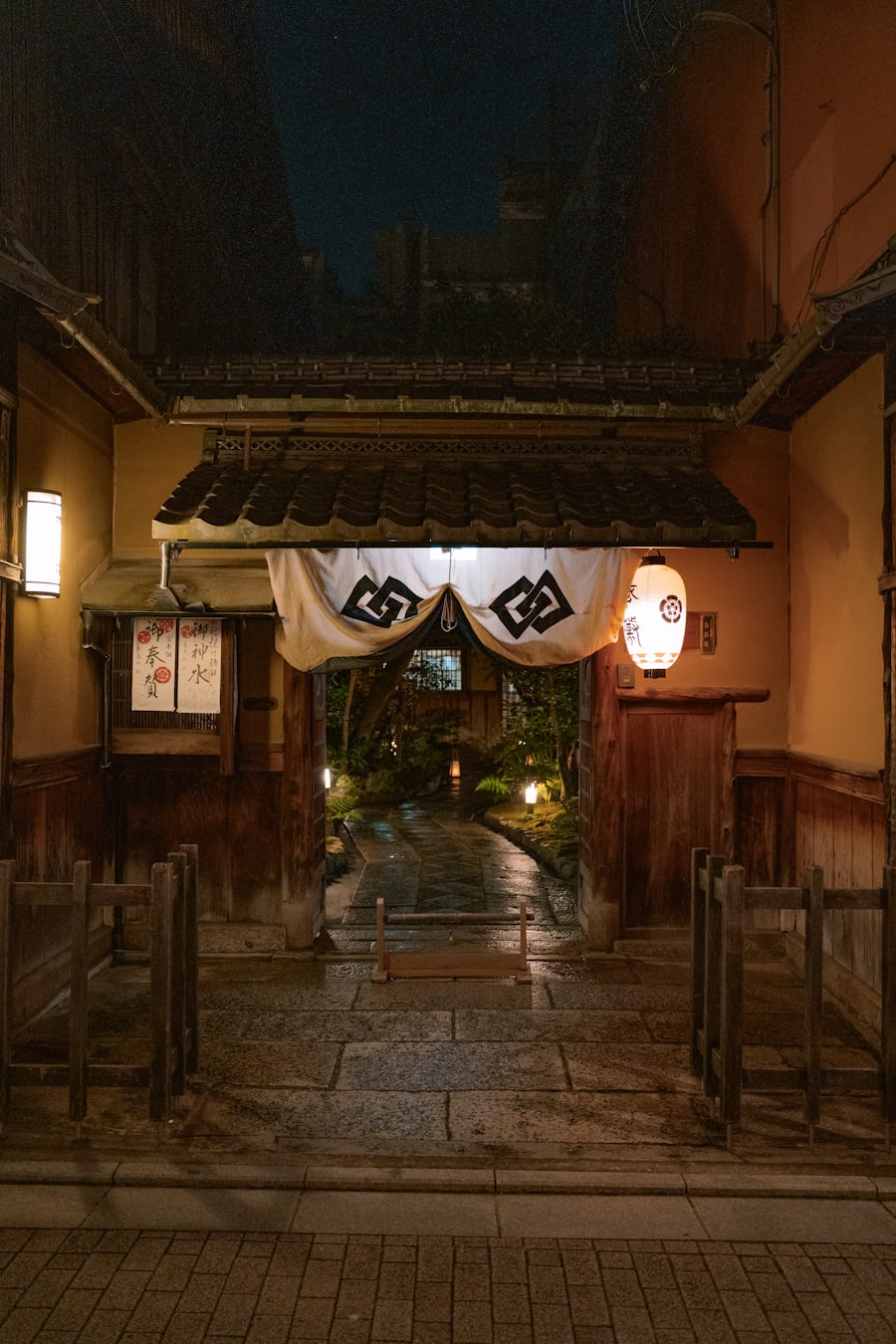 夜、あかりの灯った蒸庭の入口。のれんの奥に石畳の小路と坪庭がつづく
