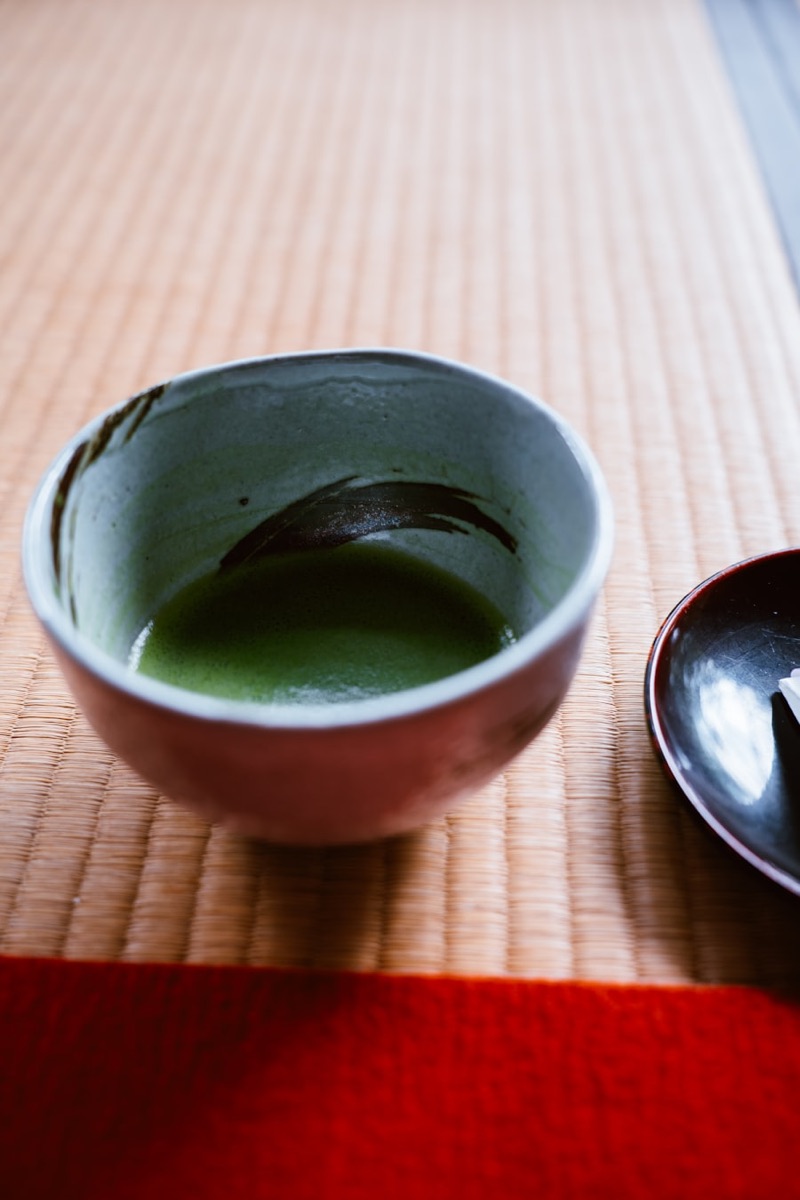 畳の上の茶碗に点てられたお薄と、漆の菓子皿